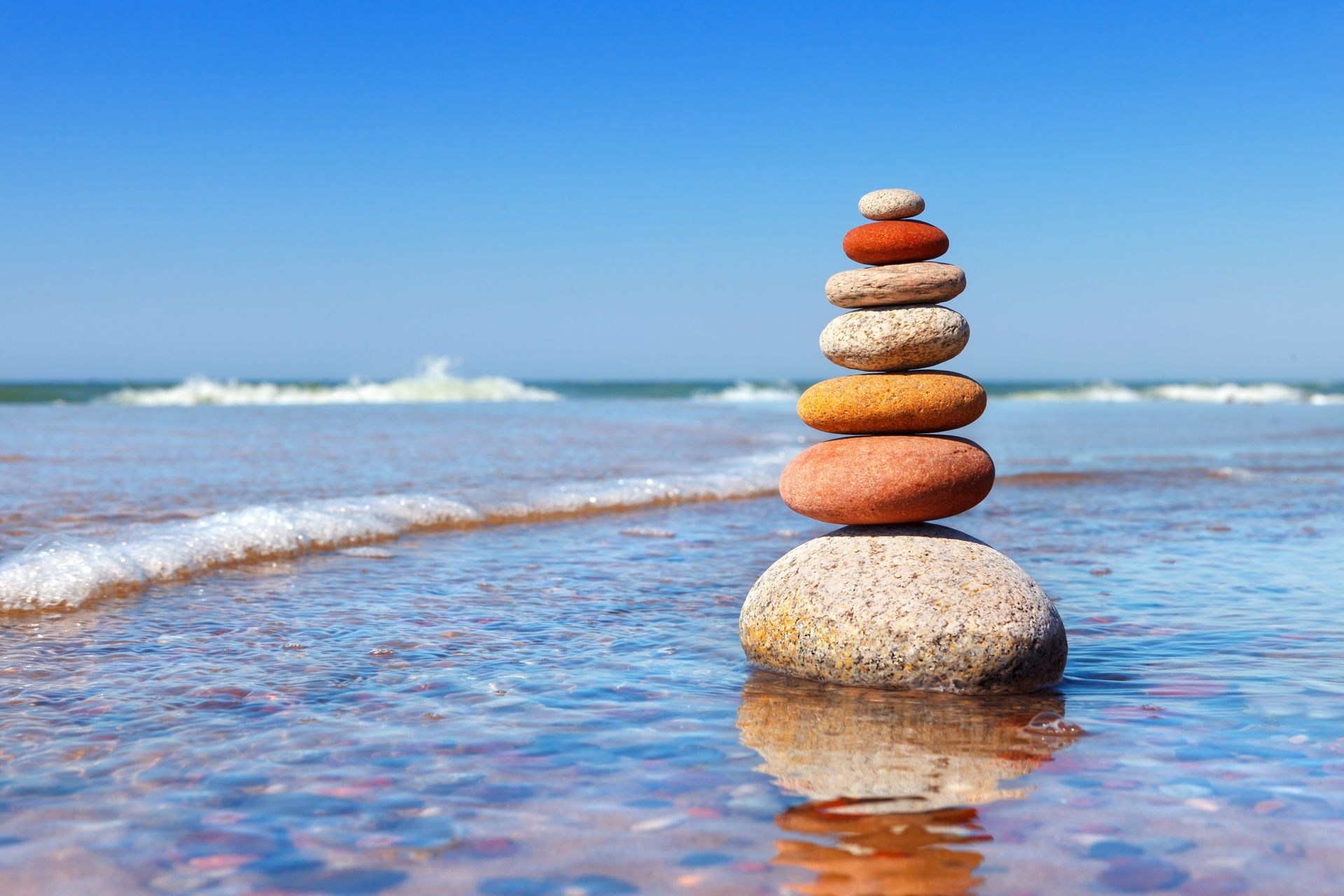 Rock zen pyramid of colorful pebbles standing in the water on the background of the sea. Concept of balance, harmony and meditation